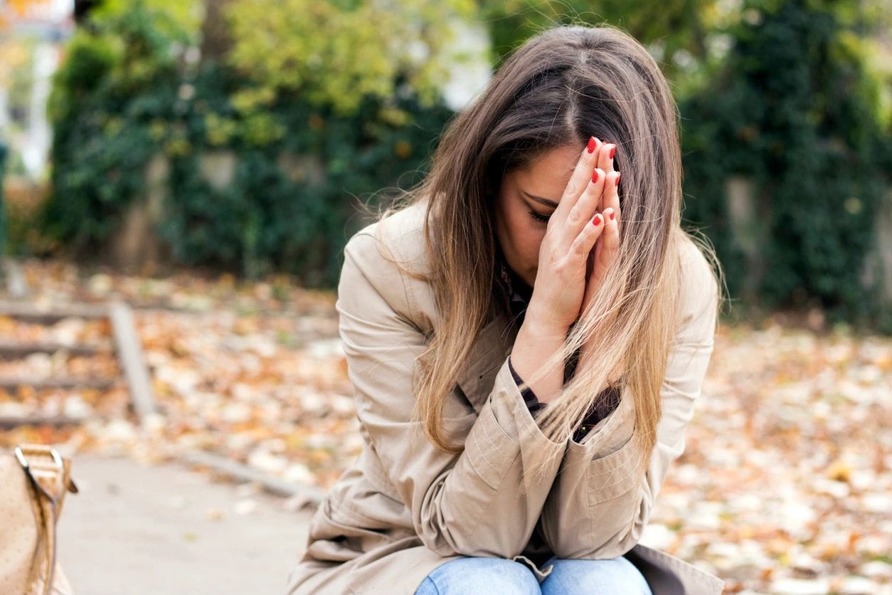 A woman sitting on the ground with her hands in front of her face.
