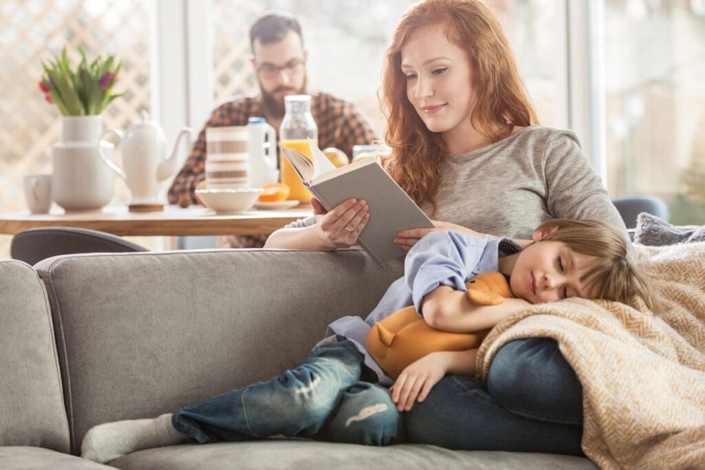 A woman and child sitting on the couch reading.